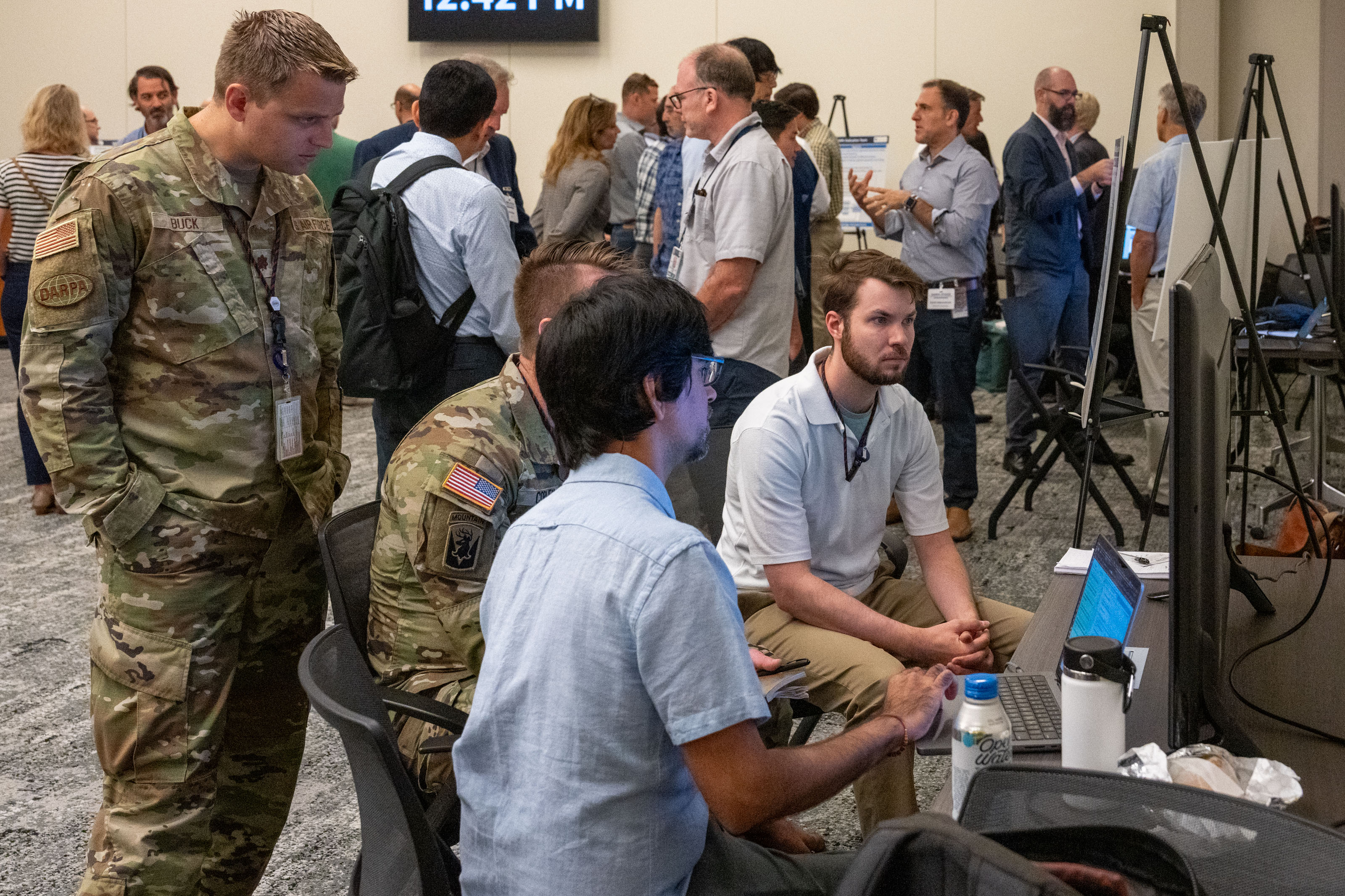 Four men staring at a laptop and television screen
